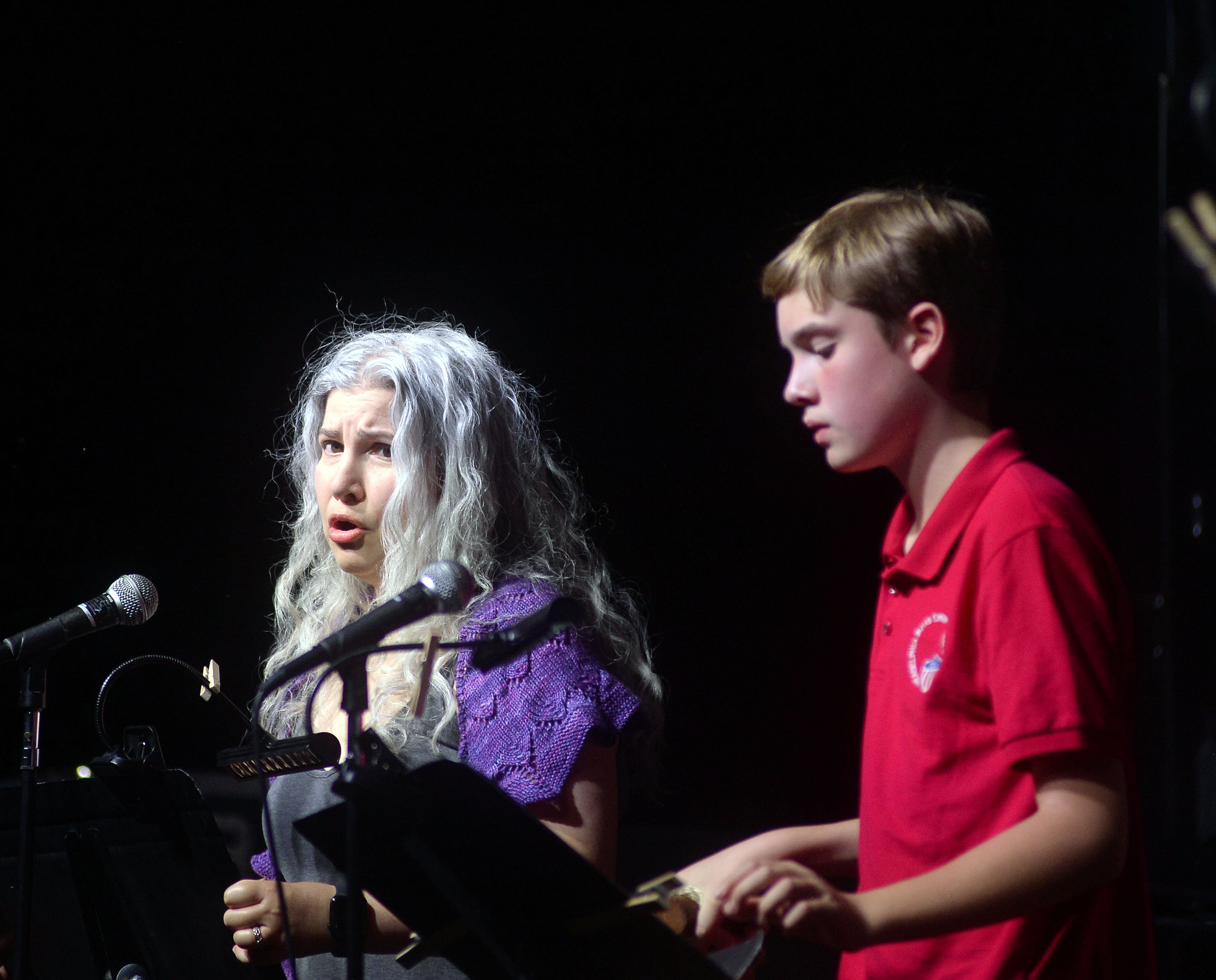 Maren Montalbano, playing The Mother, singing into a microphone, standing next to a young boy, Ethan Monberg, who plays Amahl.
