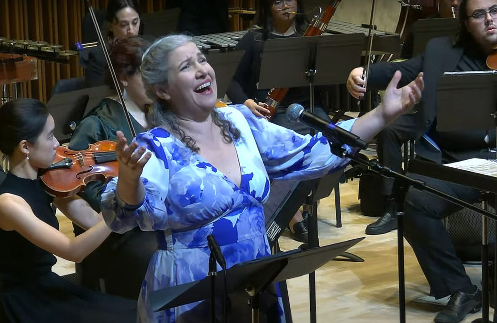 woman wearing a blue and white dress singing in front of an orchestra